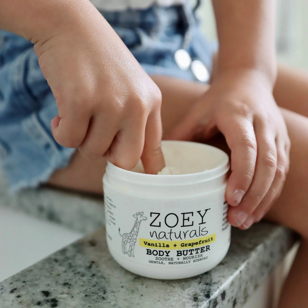 Child's hands interacting with a jar of Zoey Naturals body butter on a countertop.